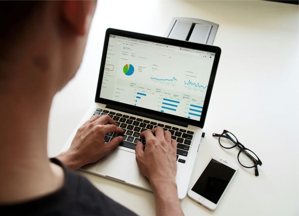 Man on laptop that has Google Analytics on the screen with a phone and glasses also on the desk.